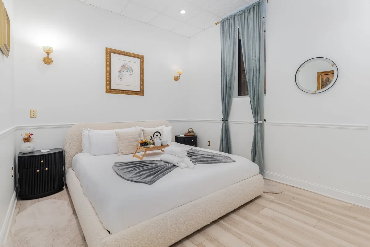 A sophisticated king bedroom with a plush bed dressed in soft bedding, decorative wall art, and a nightstand topped with a small plant. The room’s ambiance is serene and inviting, ideal for relaxing evenings or a restful night’s sleep.