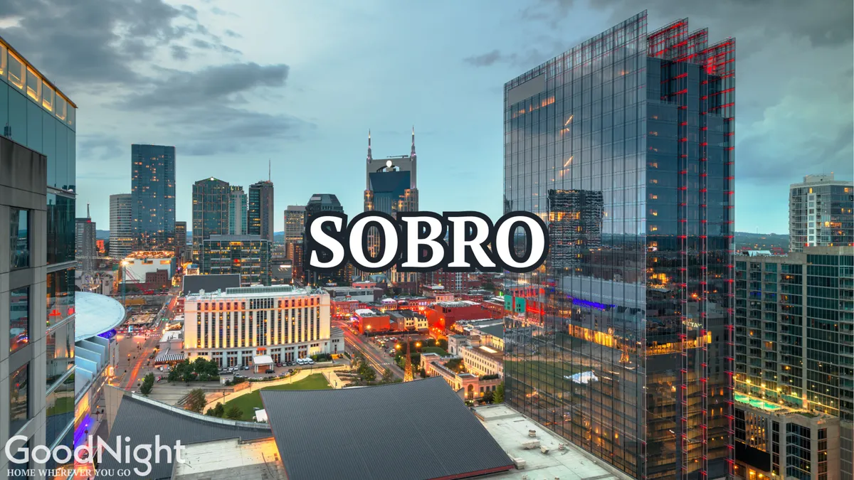 A vibrant view of the Nashville city skyline at dusk, with illuminated buildings and the bold 'SOBRO' sign. The image encapsulates the excitement and energy of downtown nightlife and the allure of exploring nearby Broadway bars and music venues.