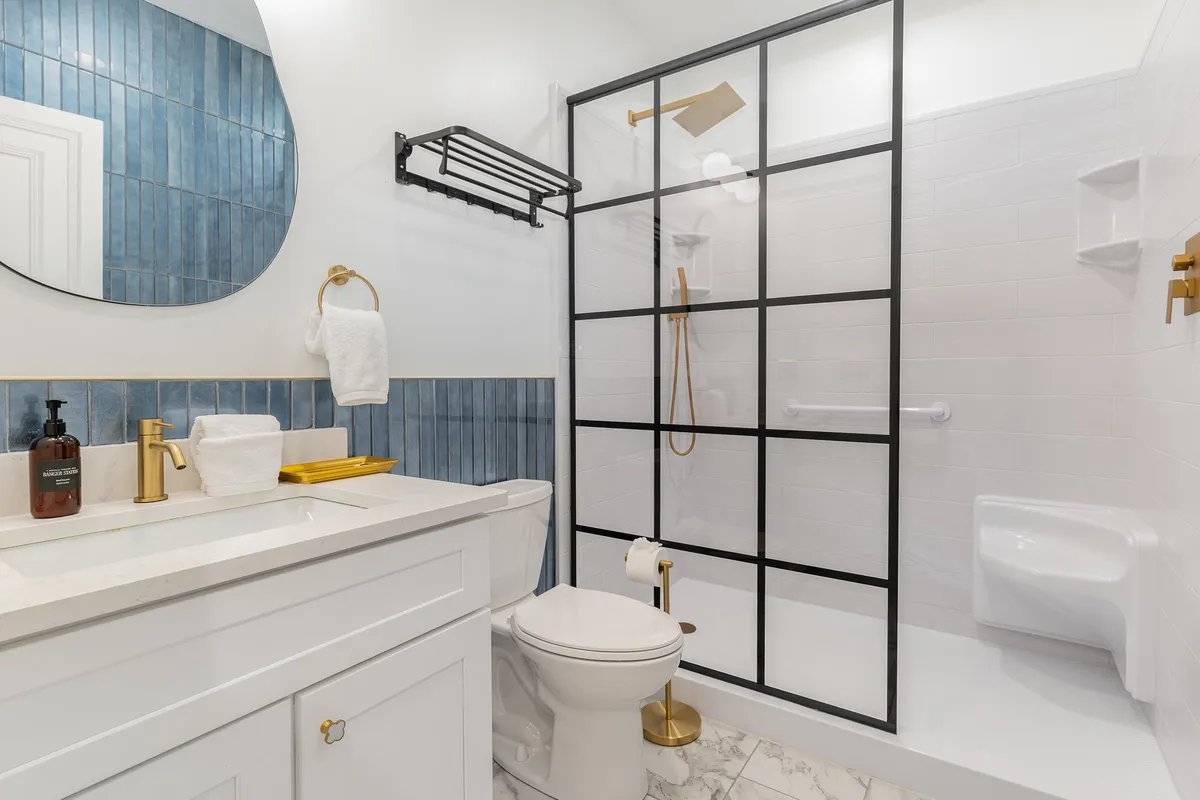 A modern ensuite bathroom with a vanity and sink, blue tile backsplash, gold fixtures, and a walk-in shower area. The clean lines and stylish details evoke a sense of luxury and rejuvenation, with everything needed for a refreshing routine.