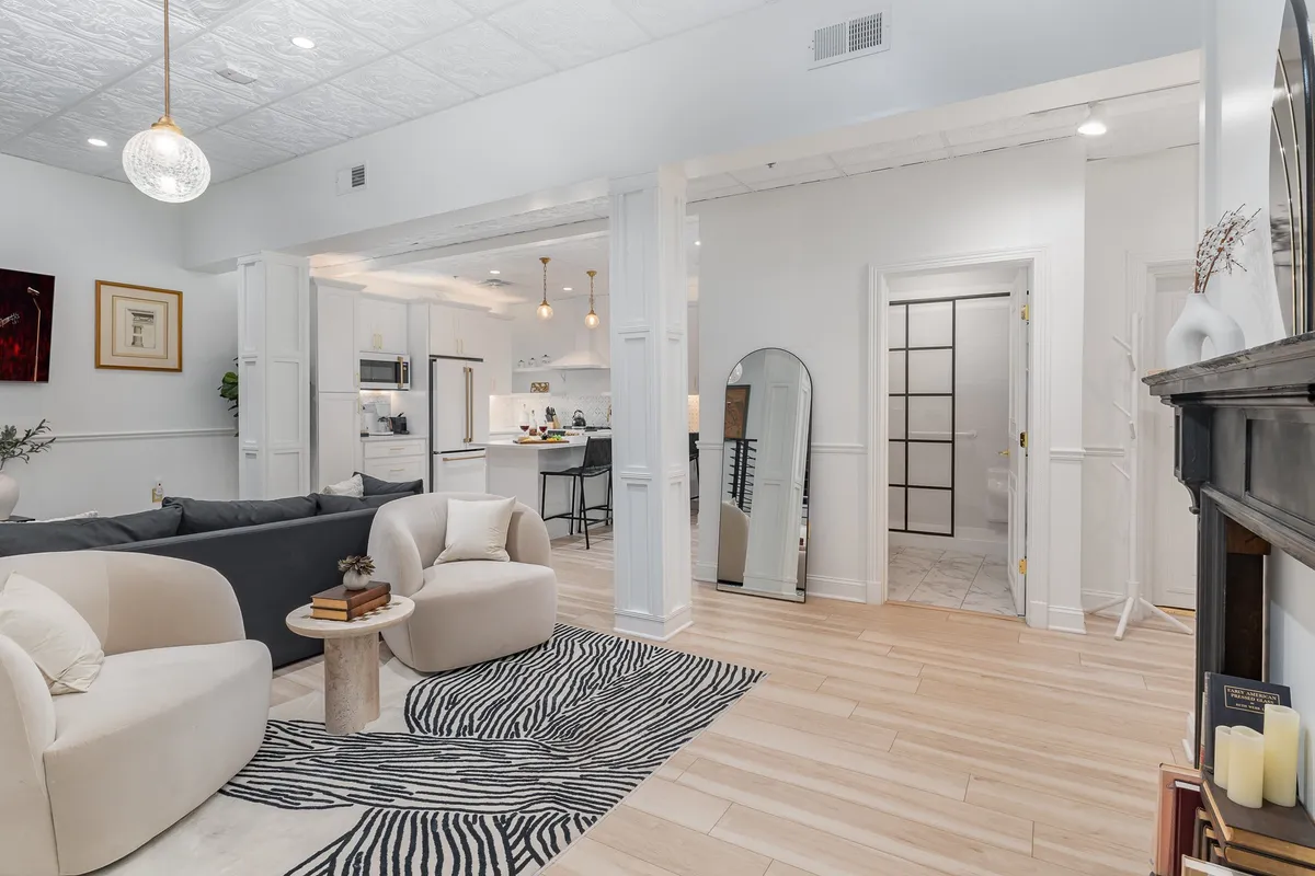 A cozy living area with a stylish coffee table, modern sofa, zebra print rug, and a view into a sleek kitchen. The open-plan layout encourages group gatherings, conversation, and convenient access to amenities.