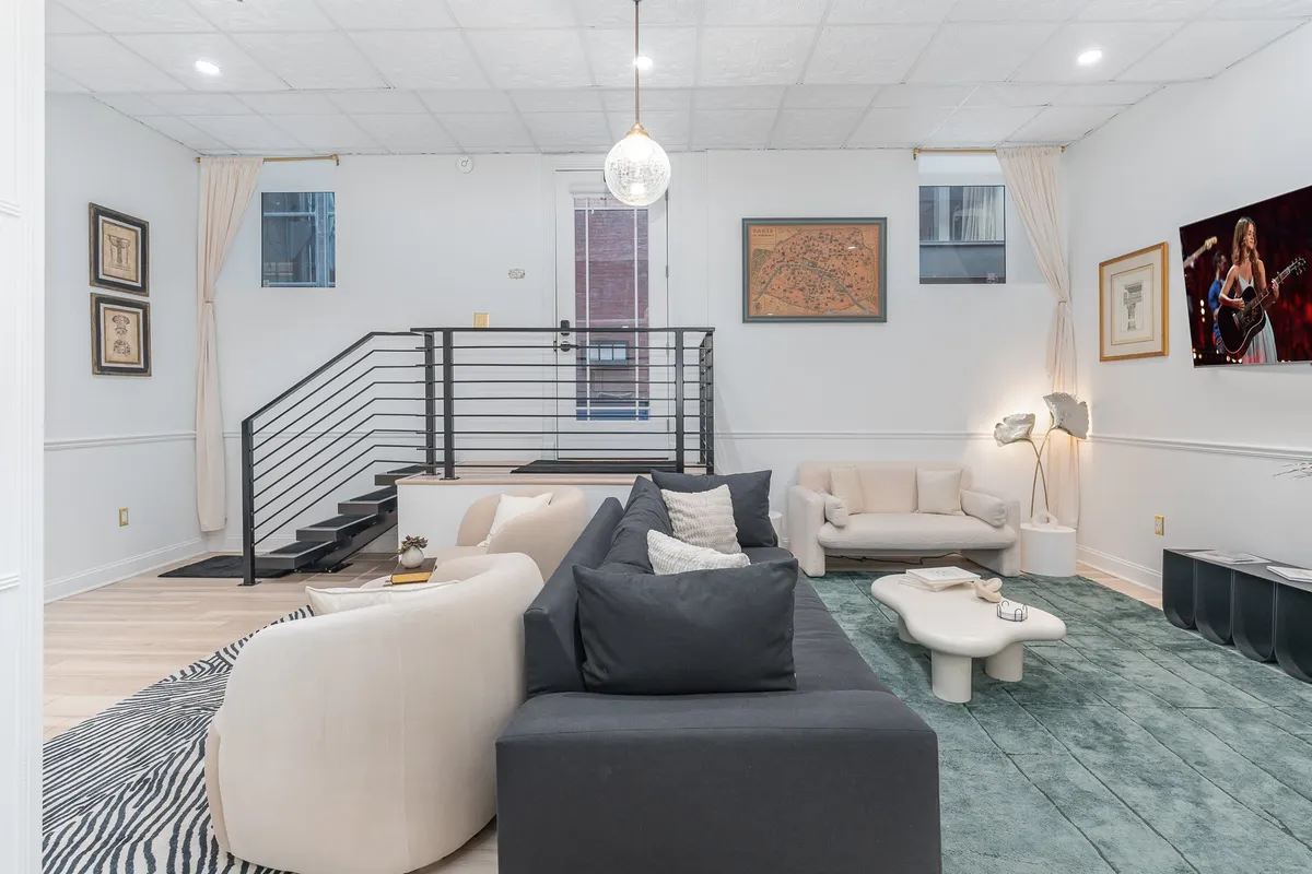 A contemporary seating area with a plush sofa, staircase, wall-mounted artwork, and a television. The open layout and modern décor set a tone of chic comfort and flexibility—key elements in the described ambiance, offering another view of the social space.