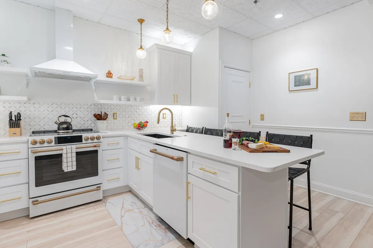 A modern kitchen featuring a central island with gold fixtures, stainless steel appliances, and cozy bar seating. The inviting space is styled for entertaining, with subtle touches hinting at both functionality and comfort, such as ample counter space and a coffee maker in the background.