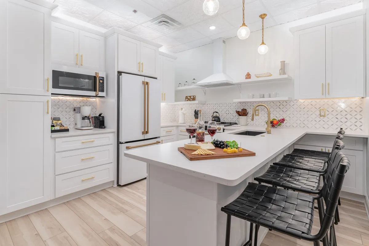 A kitchen island adorned with a charcuterie board, modern appliances, and elegant pendant lighting overhead. The textured backsplash and surrounding seating create a warm, communal vibe perfect for hosting, family meals, or wine tastings.